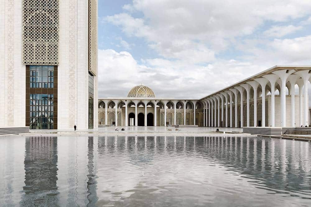 big mosque has a large decorated dome and a very tall tower with glass at the top the walls are made of light-colored stone with big arched doors and windows
