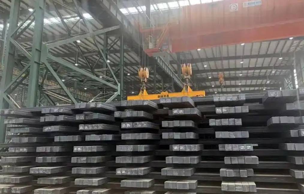  a large industrial warehouse with stacks of steel slabs being lifted by an overhead crane using heavy-duty hooks.