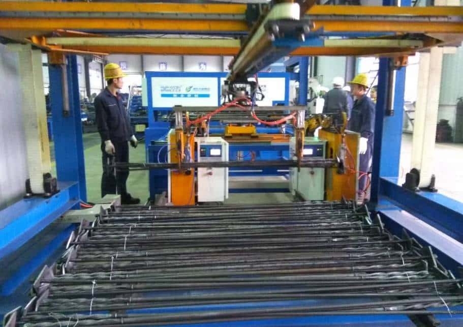 an industrial manufacturing facility where workers in safety gear are operating an automated machine handling metal rods or rebar