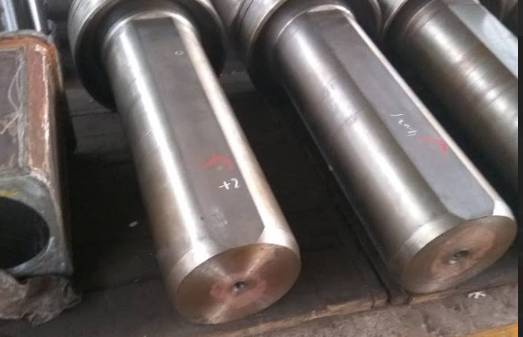  large, machined steel shafts with a polished finish, neatly arranged on a workshop floor, marked with numbers and symbols for identification or quality control.