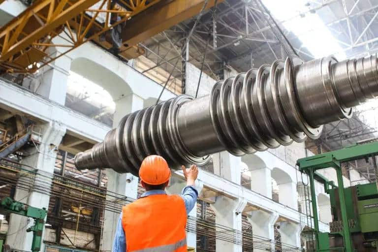 worker in a factory directs a piece of metal being moved