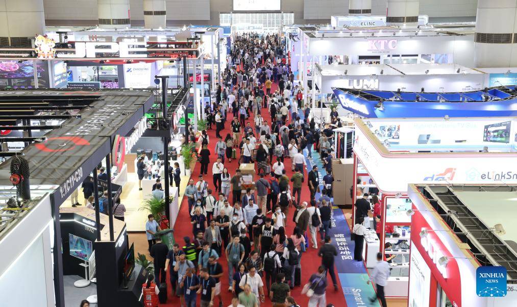Image of many booth displays and a walkway with a large group of attendees navigating around the area and some interacting with company representative in their booth.