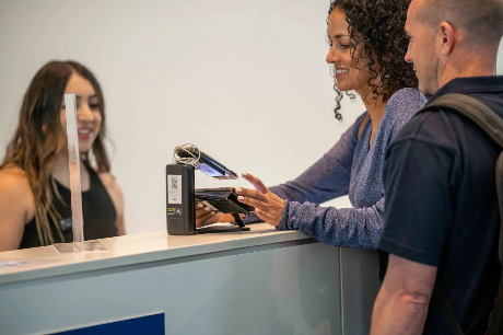 A visitor checking in at the WA Mining registration desk, tapping a digital wallet pass while a staff member smiles behind the counter