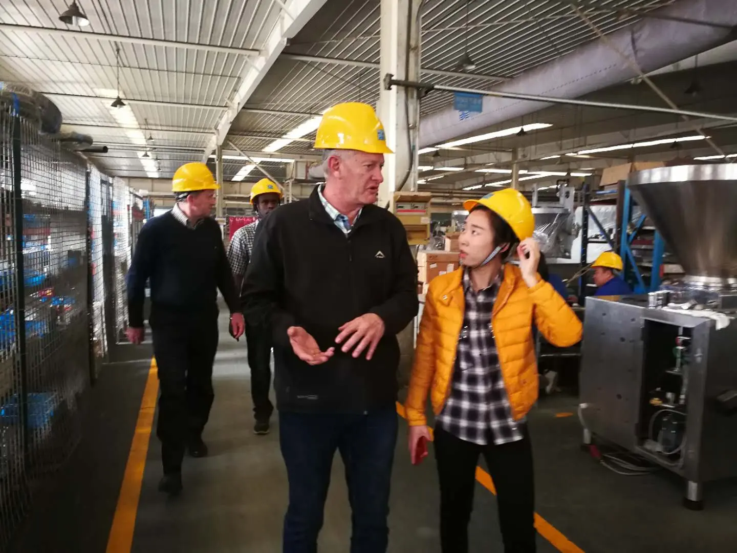 Visitors wearing hard hats walking through a Chinese equipment manufacturing factory floor past mining machinery during a CAMAL-arranged site visit