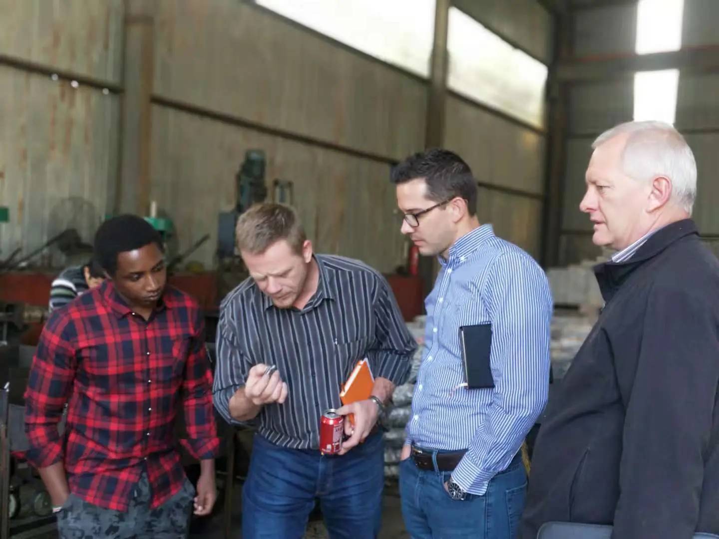 A small group examining a metal sample part inside a Chinese steel workshop during a supplier visit