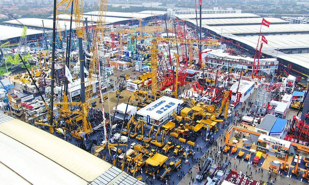 Aerial view of a large construction equipment trade show featuring cranes, excavators, loaders, and other heavy machinery across multiple exhibition areas.