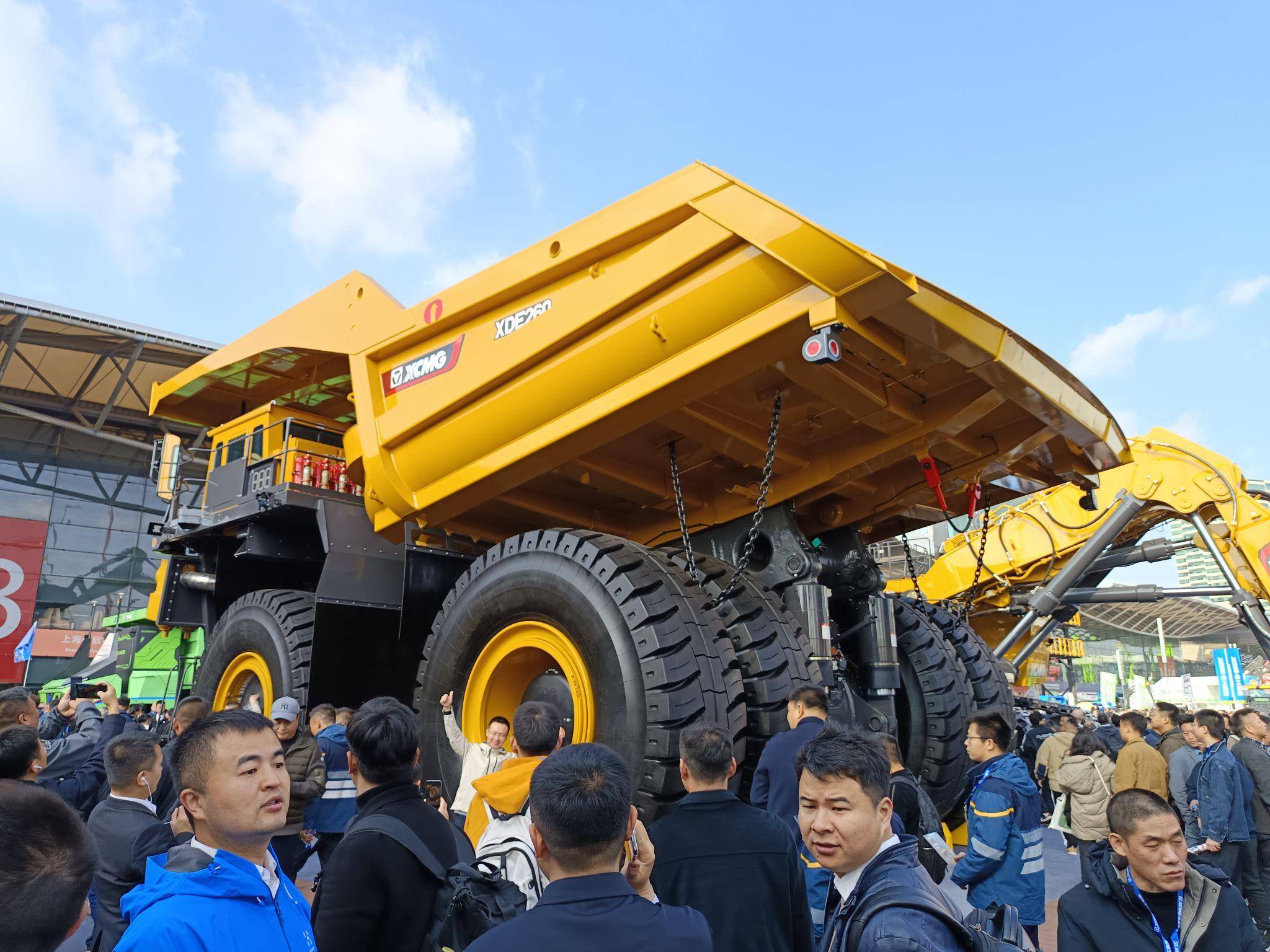 XCMG XDE130 mining dump truck displayed at a construction equipment trade show, surrounded by visitors and heavy machinery.